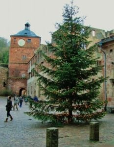 Christmas tree adorned with lights in a historic courtyard, surrounded by people and ancient stone buildings, reflecting holiday travel traditions.