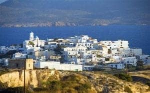 Scenic view of Adamantas, a picturesque coastal village in Milos, Greece, featuring whitewashed buildings against a backdrop of blue sea and mountains.