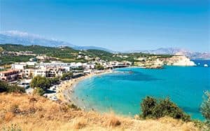 Scenic view of Almyrida beach in Crete, featuring clear turquoise waters, sandy shore, and surrounding hills, highlighting a popular travel destination for visitors seeking cultural experiences and relaxation.