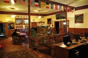 Interior view of Hilo Bay Hostel showcasing communal area with dining tables, computer stations, and international flags, highlighting amenities for travelers.