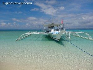 Traditional banca boat anchored on clear turquoise waters of Bohol, Philippines, under a bright blue sky, showcasing the beauty of the travel destination.