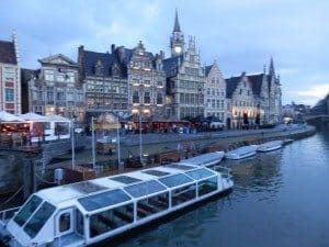 Historic buildings along the canal in Bruges, Belgium, with a boat in the foreground, showcasing the city's architecture and charm.
