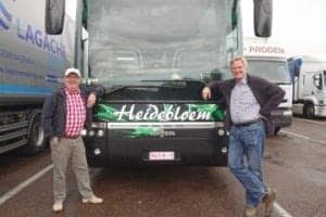 Two men posing beside a green bus with "Heidebloem" branding, highlighting bus travel experiences.