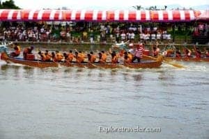 Dragon boat team competing in a race on a river, surrounded by spectators under a colorful canopy, capturing the excitement of dragon boat events and cultural experiences.