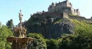 Edinburgh Castle perched on a rocky hill, surrounded by lush greenery and a decorative fountain in the foreground.