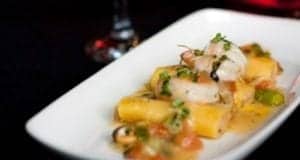 Plate of Aldente pasta with shrimp, garnished with herbs and diced vegetables, set against a dark background, showcasing culinary experiences in travel.