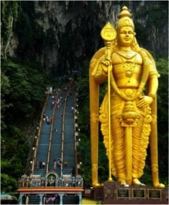 Golden statue of Lord Murugan at Batu Caves, Malaysia, with steep steps leading to the cave entrance, surrounded by lush greenery.