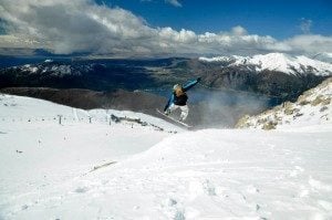 Snowboarder performing a jump on Cerro Catedral's slopes, surrounded by snow-covered mountains and a clear blue sky, highlighting the destination's winter sports appeal.