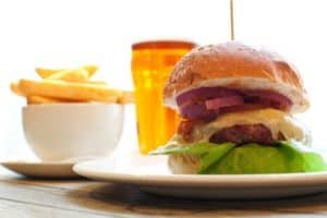 Plate featuring a gourmet hamburger with lettuce, onion, and sauce, accompanied by a side of golden French fries and an orange beverage.