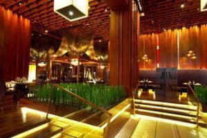 Luxurious dining interior in Bangkok featuring wooden decor, ambient lighting, and greenery, emphasizing the city's vibrant culinary scene.
