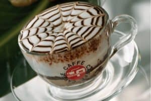 Coffee cup with decorative foam art, showcasing a spider web design, representing cafe culture and dining experiences on ExploreTraveler.