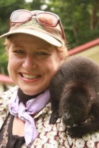 Dog sitting on a woman's shoulder, smiling, in a natural setting, promoting travel and lifestyle experiences related to pets.