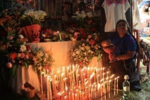 Woman beside floral arrangements and lit candles at a vibrant market, showcasing floral design and cultural significance in travel experiences.