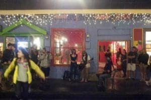 People enjoying a vibrant night scene in Hilo, Hawaii, with colorful storefronts and festive lights, capturing the lively atmosphere of the local culture and nightlife.