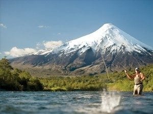 Man fly fishing in a river with a snow-capped mountain backdrop, illustrating the beauty of outdoor recreation and fly fishing experiences.