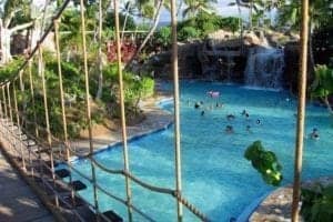 Tropical pool area at Halana Hale featuring a waterfall, lush greenery, and people enjoying the water.