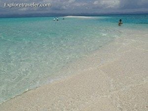 Scenic beach landscape with turquoise waters, sandy shore, and distant figures enjoying the serene environment, highlighting travel experiences and beach destinations.