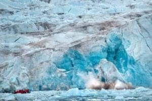 Iceberg calving into the water with a small boat nearby, showcasing stunning blue ice formations, relevant to ExploreTraveler's focus on travel and natural wonders.