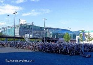 Bicycles parked in a large bike parking area near a modern building in Amsterdam, highlighting the city's cycling culture and travel experiences.