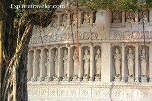Facade of intricately carved stone wall featuring multiple Buddha statues, surrounded by lush greenery, emphasizing cultural travel experiences.