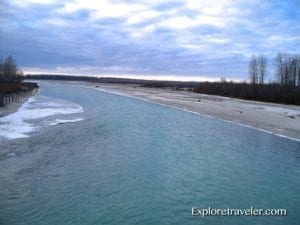 Talkeetna River floodplain in Alaska, featuring turquoise water, sandy banks, and overcast skies, highlighting the area's natural beauty and travel significance.