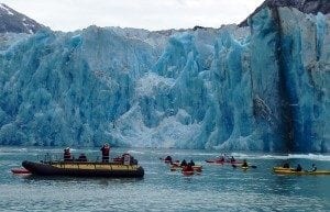 Kayakers and a boat navigating near a massive blue glacier, showcasing a stunning travel destination for adventure seekers.