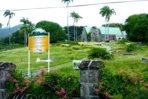 Cruise port landscape featuring a historical site with ruins, palm trees, and a informational sign in a lush green setting.