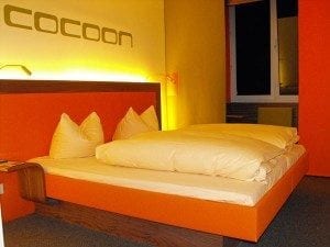 Modern bed frame in vibrant orange and yellow room with large pillows and soft bedding, highlighting travel accommodation options.