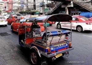 Colorful tuk-tuk in busy city street with red taxis, representing travel and local transportation options.