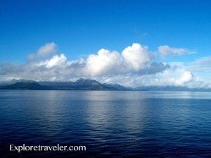 Scenic view of Heaven Lake with calm waters reflecting clouds and mountains under a blue sky, showcasing the natural beauty highlighted by ExploreTraveler.