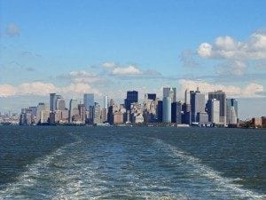 View of a city skyline from a ferry, showcasing urban architecture against a blue sky with clouds, relevant to travel insights and ferry experiences.