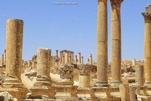 Ancient Roman ruins in Jerash, featuring tall, weathered columns and stone structures under a clear blue sky, illustrating the historical significance of the site.