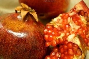 Pomegranate fruit with vibrant red seeds, showcasing a whole fruit and a sliced piece, emphasizing culinary experiences in international food culture.