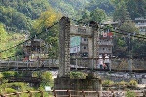 Suspension bridge in Hsinchu County, Taiwan, connecting Aboriginal Hakka villages, surrounded by lush greenery and traditional buildings.