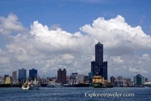 Gushan District skyline in Kaohsiung City, Taiwan, featuring modern buildings, boats on the water, and a blue sky with clouds, highlighting the area's urban landscape and travel appeal.