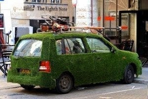 Car covered in grass, parked in urban setting, highlighting green space initiative in Israeli city, showcasing unique blend of nature and urban life.