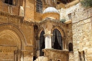 Holy Sepulchre church exterior featuring intricate stone architecture, large arched windows, and a domed structure, highlighting its historical significance as a key religious site for travelers.