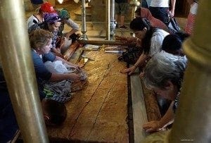 Group of travelers examining a large wooden artifact in a historical site, showcasing engagement with cultural heritage and travel experiences.