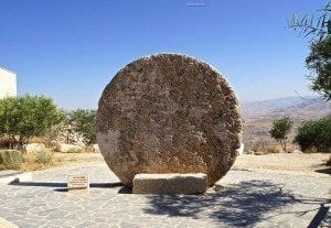 Ancient stone wheel at Mount Nebo, a significant historical site in the Holy Land, surrounded by olive trees and scenic views.