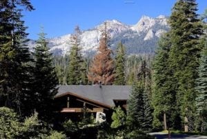 Lodge nestled among tall evergreen trees with snow-capped mountains in the background, highlighting the natural beauty of Fir as a travel destination.