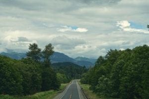 Scenic road leading toward Mount Rainier, surrounded by lush greenery and mountains under a cloudy sky, ideal for exploring Washington backroads.
