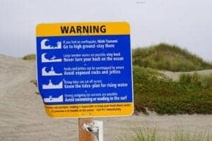 Warning traffic sign in Northern California with safety instructions for beachgoers about large waves and rip currents, emphasizing caution and awareness.