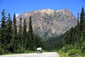 Scenic view of a highway surrounded by tall evergreen trees and a majestic mountain in the Fir area of Washington, highlighting the region's natural beauty and travel opportunities.