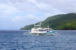 Boat anchored in clear waters near lush green hills, representing diving opportunities in the Philippines.