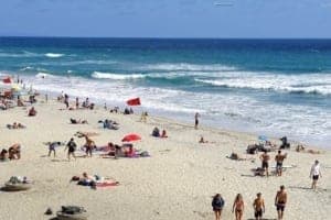 Oceanside California beach scene with sunbathers, umbrellas, and surf, highlighting a popular travel destination for leisure and fun.