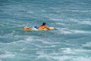 Man lying on a surfboard in the ocean, enjoying beach activities in Oceanside, California.