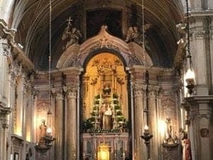 Interior view of the Church of Santa Maria Basilica in Lisbon, showcasing ornate architecture, a central altar with a statue, and decorative lighting elements.