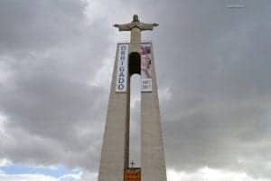 National Sanctuary of Christ the King statue in Lisbon, Portugal, towering over a cloudy sky, showcasing its monumental architecture and significance as a travel landmark.