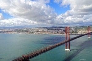 Ponte 25 de Abril Bridge spanning the Tagus River in Lisbon, Portugal, with a backdrop of blue skies and clouds.