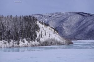 Snow-covered mountain and trees along the Robertson River in Alaska, showcasing the scenic beauty of the Eastern Alaskan Range.